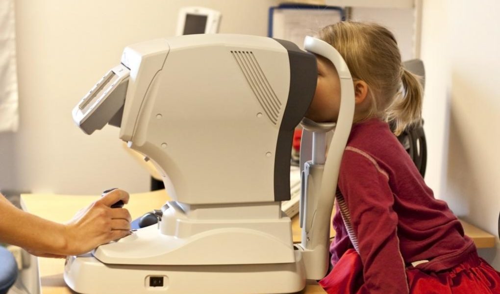 Eye doctor using eyesight testing equipment to treat a young patient