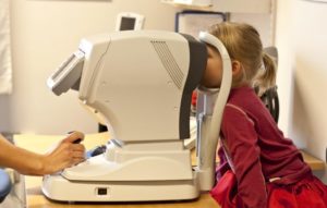 Eye doctor using eyesight testing equipment to treat a young patient